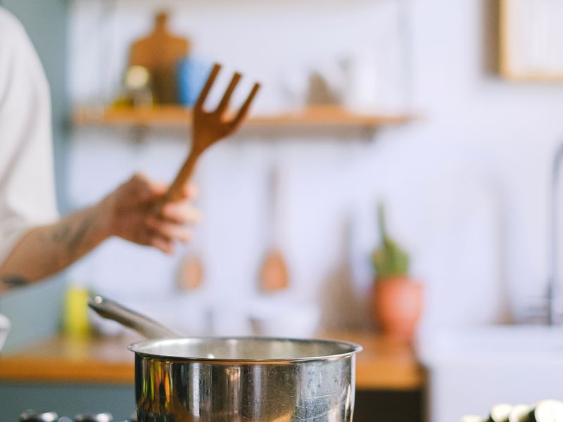 Cook holding a wooden fork over a pot in a bright kitchen