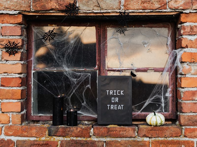 Window decorated with cobwebs and a trick-or-treat sign