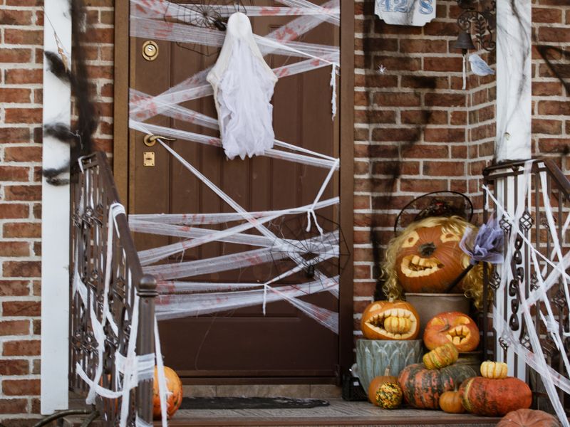 Front door decorated with webs, a ghost, and pumpkins