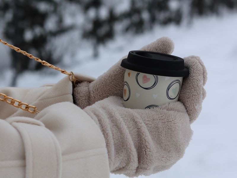 Mittened hands holding a warm cup in the snow