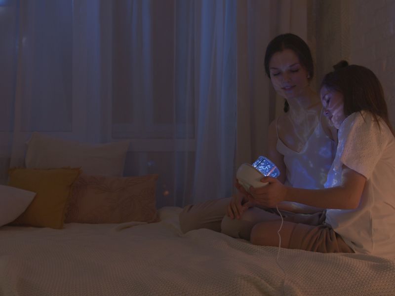 Mother and daughter in a bedroom lit by a star projector